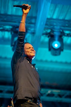 Energetic performance of a male singer raising his arm on stage under blue lights.