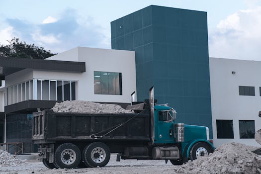 A dump truck loaded with materials parked near a modern building in Belize.