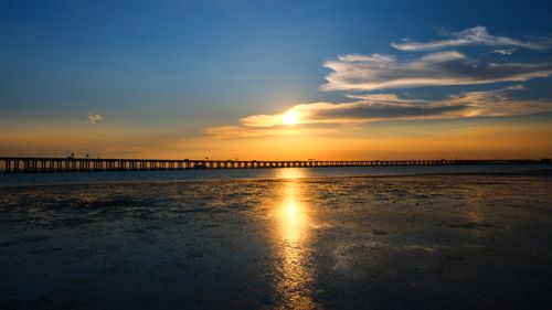 Free A breathtaking sunset over a long pier with golden reflections on the calm sea. Stock Photo