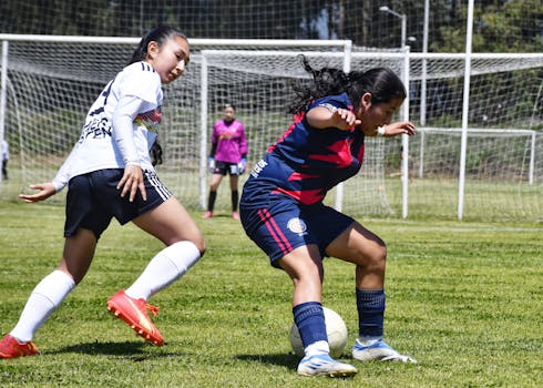 Two female football players in action on a sunny day at the soccer field.