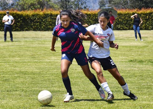 Two female soccer players competing intensely on a sunny outdoor field, showcasing team spirit and athleticism.