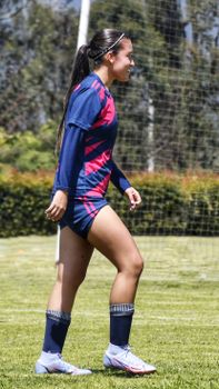 Young woman football player in sports uniform walking on grass field during daytime.