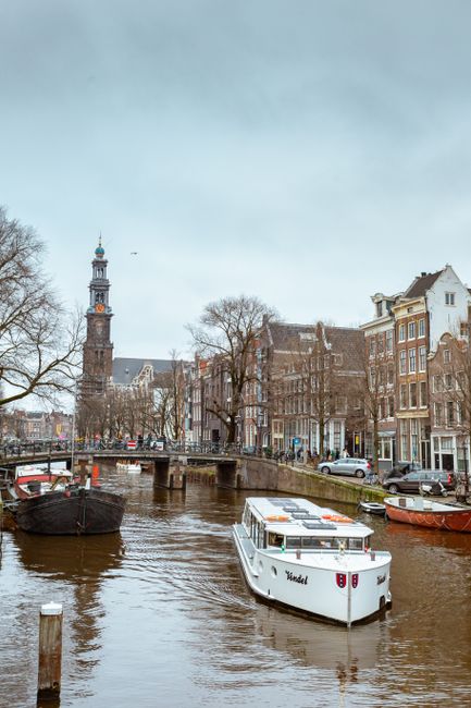 Charming view of an Amsterdam canal featuring historic buildings and boats on an overcast day.