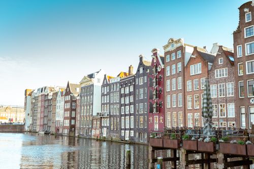 Free Scenic view of Amsterdam's iconic canal houses reflecting in calm waters under a clear sky. Stock Photo