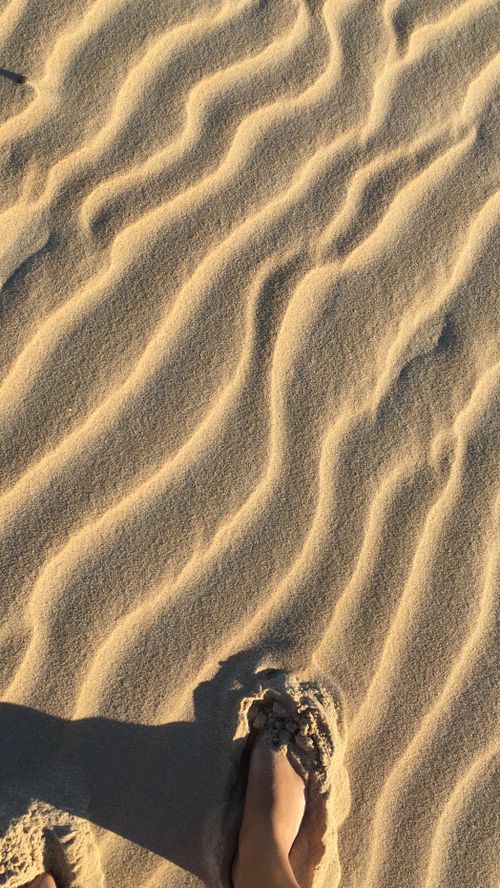 Free A foot in sand creating ripples under warm sunlight, top view. Stock Photo