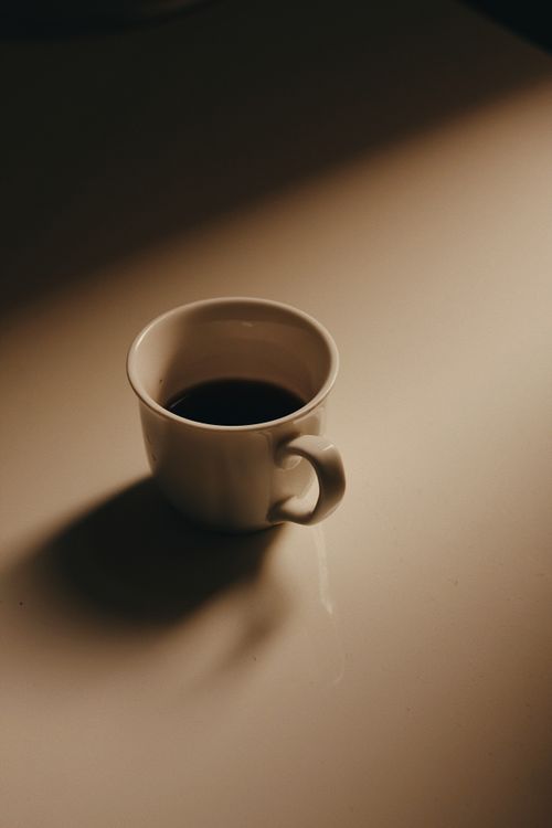 Free A single coffee cup casting a shadow on a warm beige surface, creating a tranquil ambiance. Stock Photo
