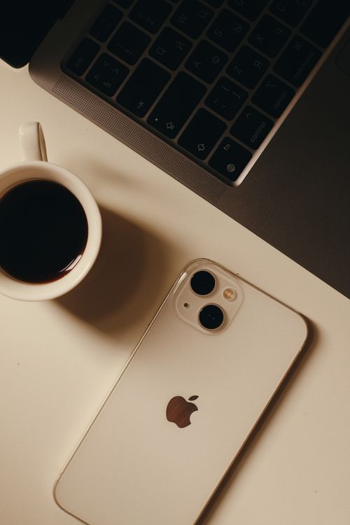 Free A sleek setup featuring a cup of coffee, smartphone, and laptop on a desk. Stock Photo