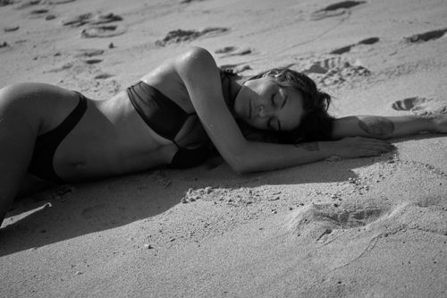 Free A woman in a bikini lying on a sandy beach in a serene black and white portrait. Stock Photo