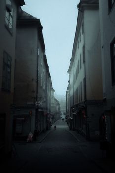 A narrow urban alley under a misty, overcast sky, creating a moody atmosphere in a cityscape.