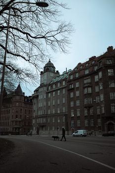 A moody, overcast city street scene featuring historic buildings and a person walking a dog.
