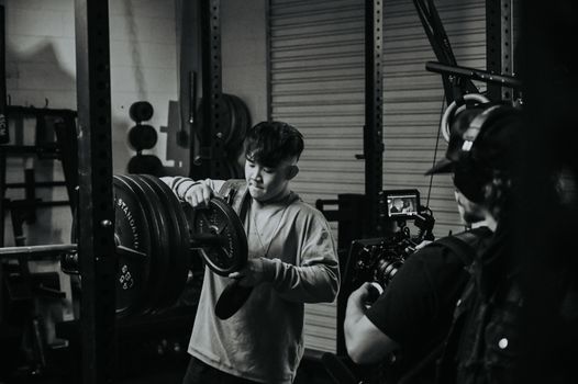 A man focuses while adjusting weights in a gym during weightlifting session captured in monochrome.