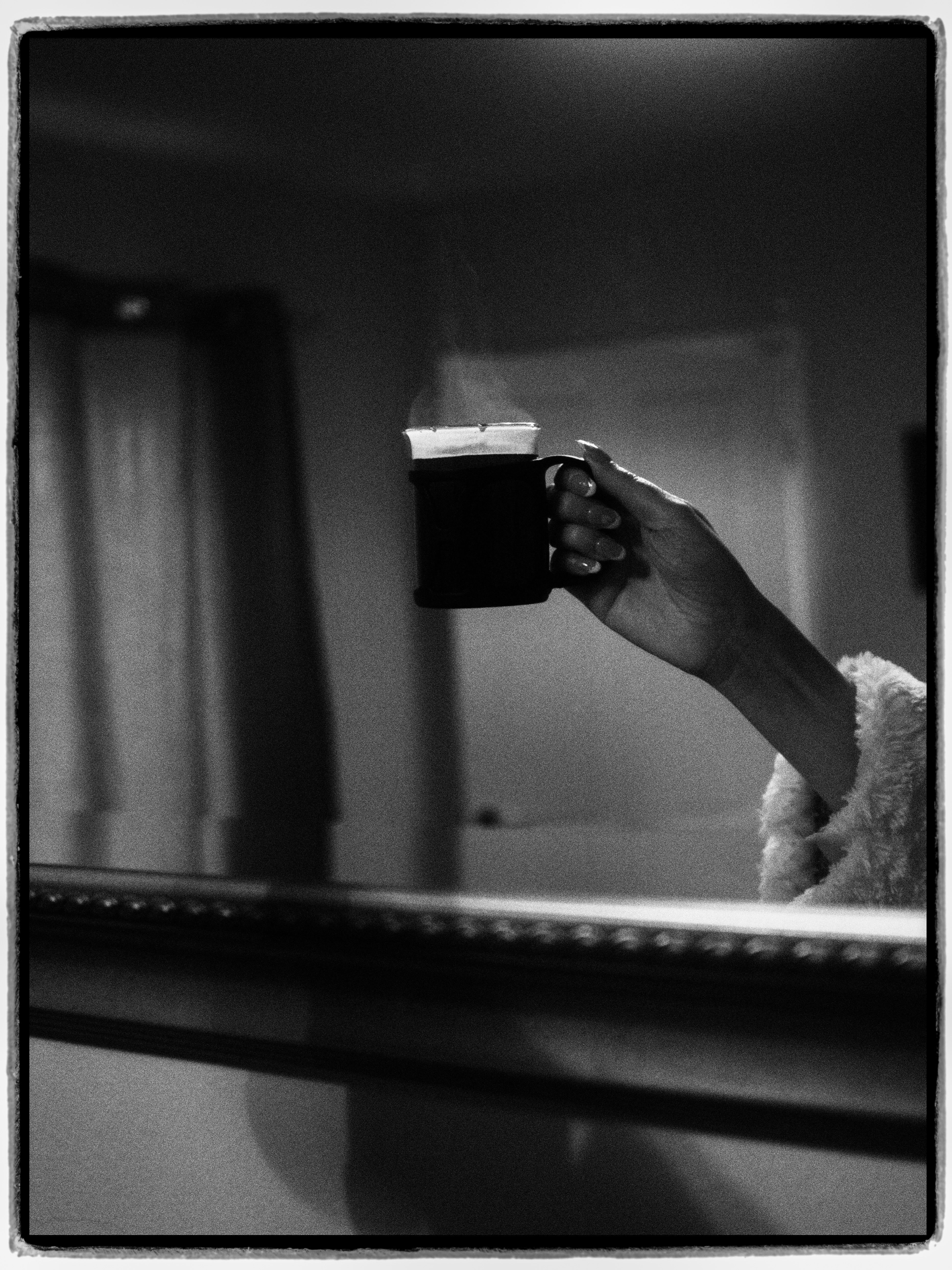 A hand holds a steaming mug in a cozy monochrome setting.