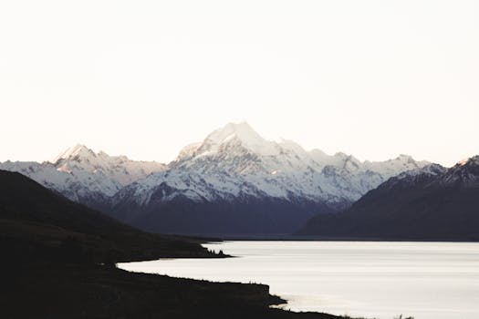 Breathtaking view of a snow-capped mountain range reflecting on a serene lake at dusk.