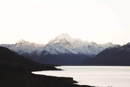 Free Breathtaking view of a snow-capped mountain range reflecting on a serene lake at dusk. Stock Photo