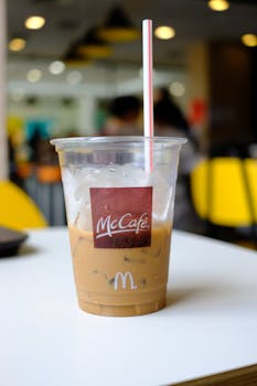 Chilled iced coffee in McCafe plastic cup with straw on table.