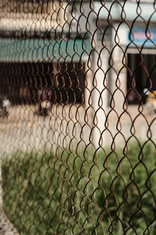 Free Detailed shot of a chain link fence with blurred urban background, indicating enclosure and protection. Stock Photo