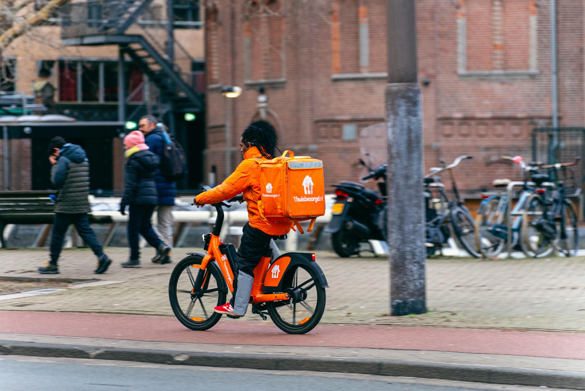 Bike courier in orange uniform delivers food on Amsterdam street.