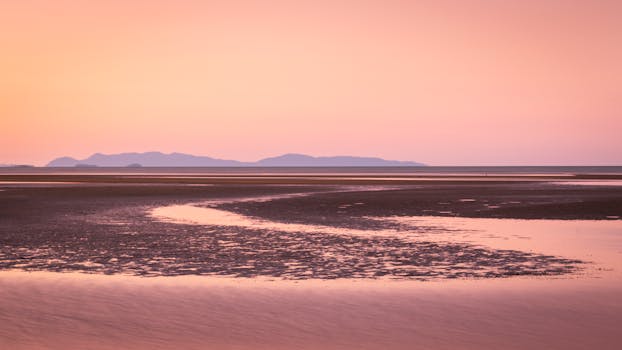 Tranquil beach scene with a vivid sunset and distant mountains, perfect for travel inspiration.