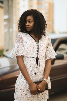 Fashionable woman in white lace dress stands outdoors with a contemplative expression.