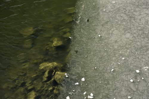 Free Aerial view of a frozen river contrasting with a rocky shoreline. Stock Photo
