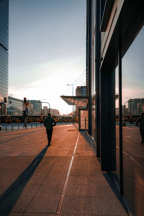 Free A person walks along a modern city street in Warsaw during sunset, capturing a lively urban atmosphere. Stock Photo