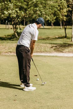 Male golfer wearing a cap putting the ball on a sunny day at the golf course.
