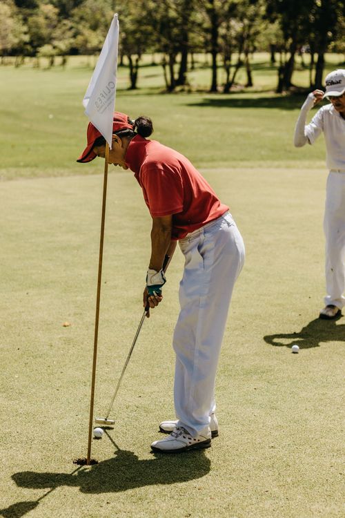 Free Two golfers enjoying a sunny day game, focusing on a precise putt on green. Stock Photo