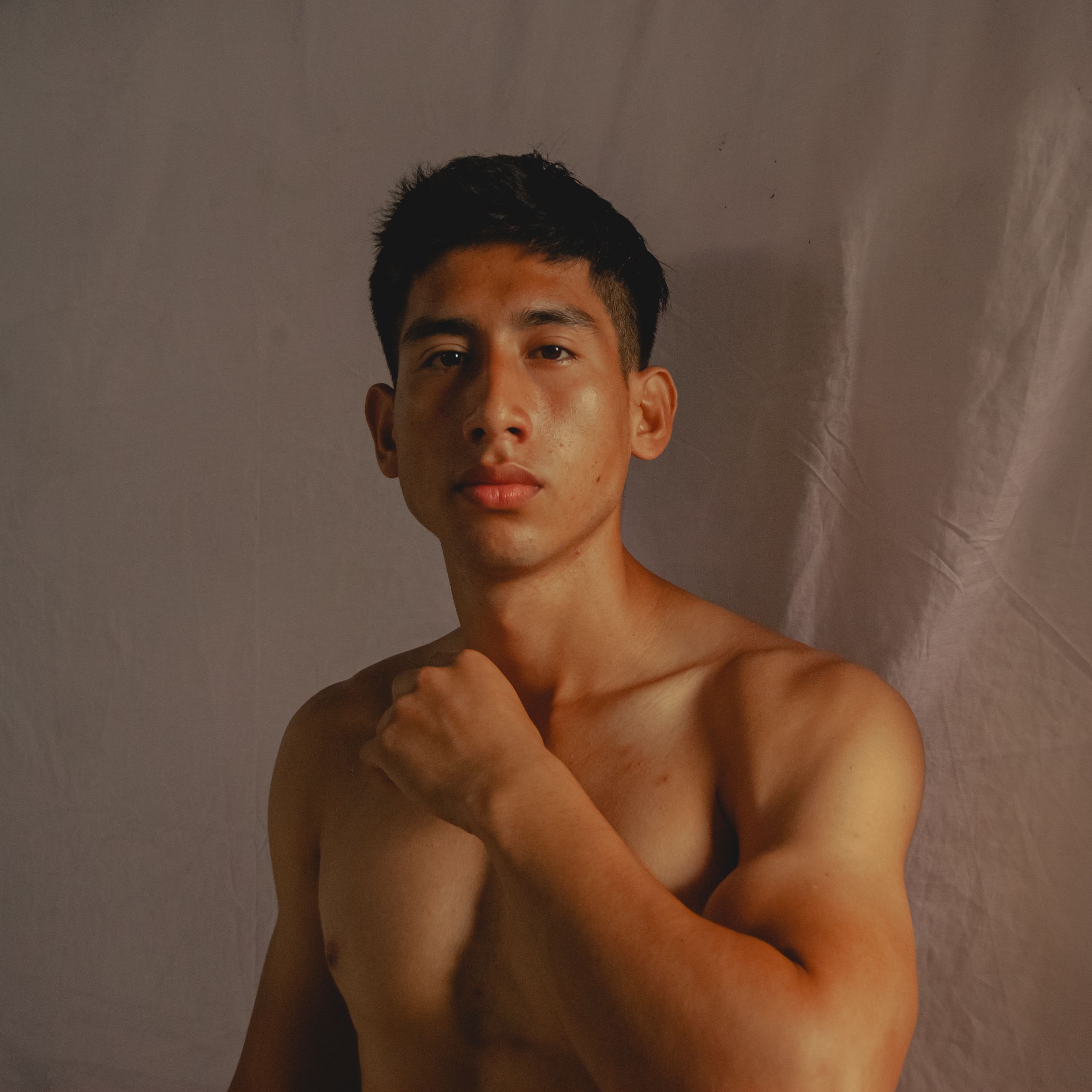 Confident young man posing shirtless against a simple backdrop.