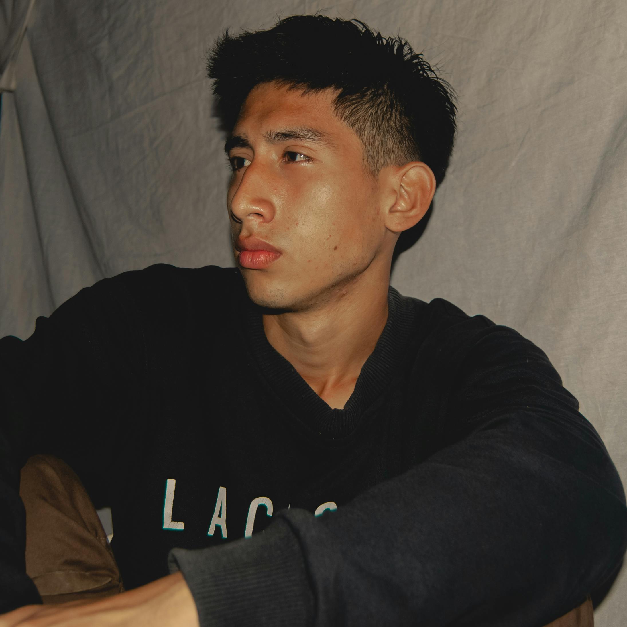 Close-up portrait of a young man with short hair in a moody indoor setting.