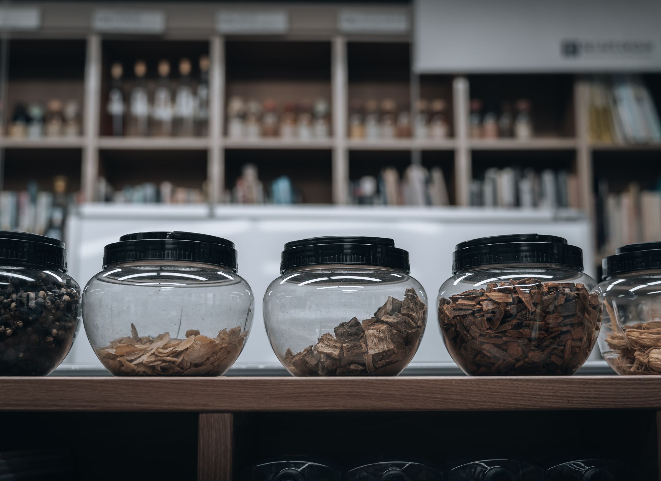 Glass apothecary jars of dried herbs and roots lined up on a wooden shelf.