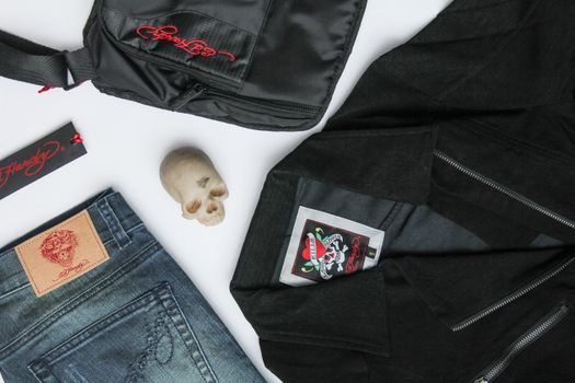Top view of stylish black jacket with skull detail placed on white table with bag and jeans