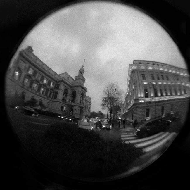 Black and white fisheye capture of city traffic and historic architecture.
