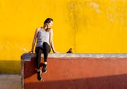 在葡萄牙辛特拉，一名年轻女子靠着充满活力的黄色墙壁，坐在户外享受阳光灿烂的日子