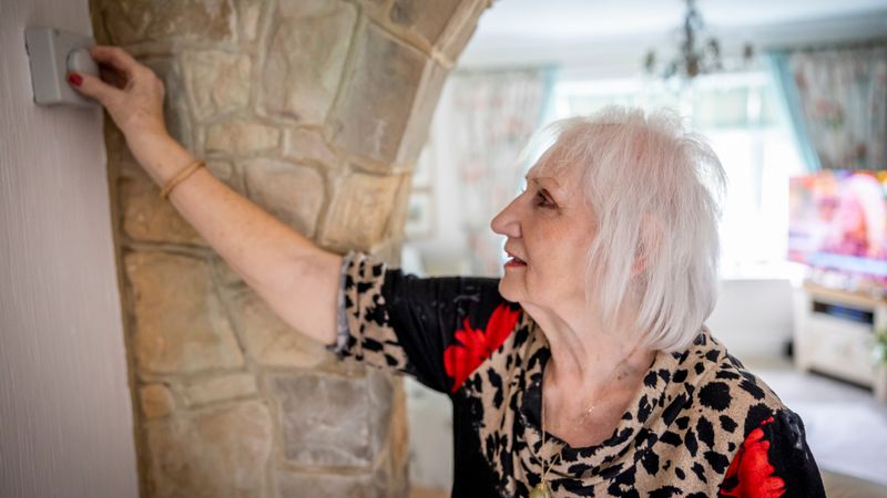 A person adjusting a smart thermostat on a wall while a small ceramic space heater runs in the background.