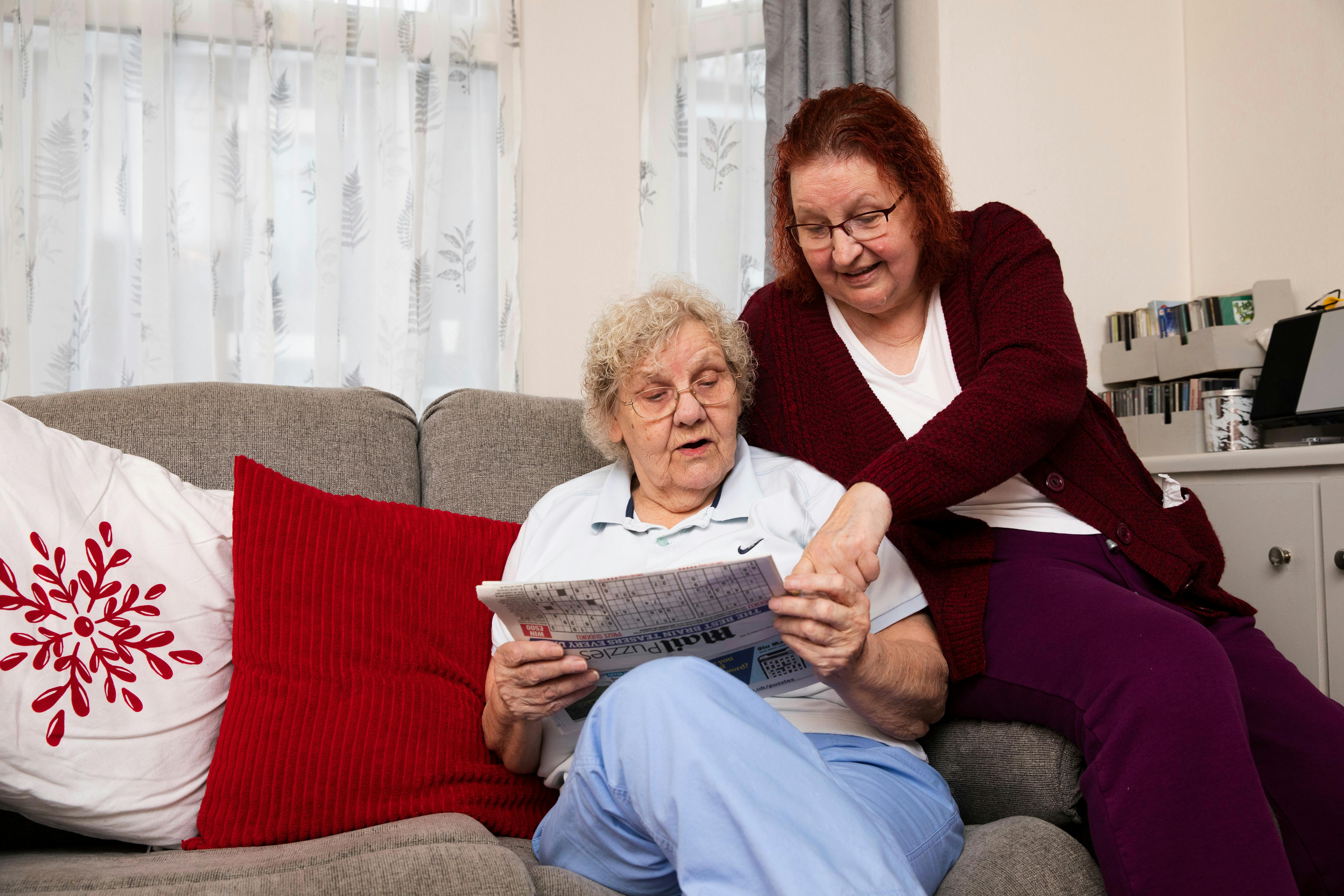caregiver reading to an elderly woman in a cozy living room