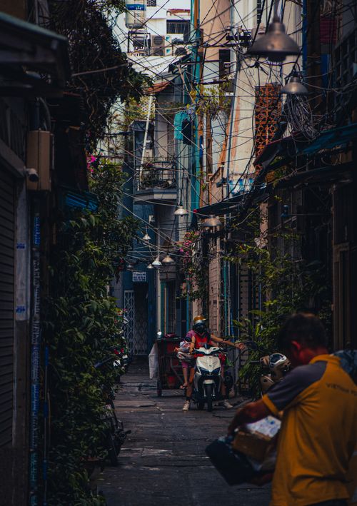 Free Cozy alleyway with people, scooters, and lush plants, showcasing urban charm. Stock Photo