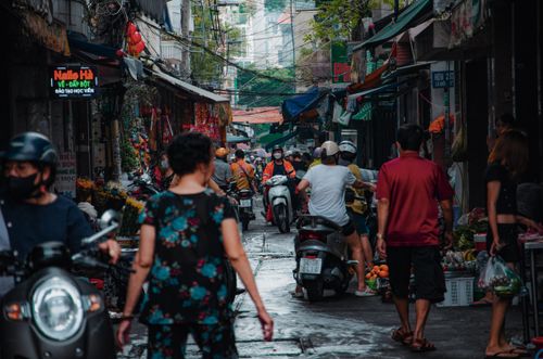 Free Lively street scene with people walking and riding scooters in a crowded urban area. Stock Photo