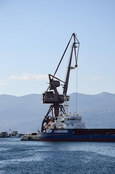 A cargo ship docked at Rijeka port with a crane against scenic Adriatic backdrop.