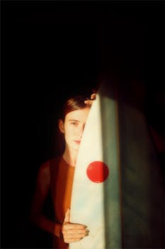 Artistic portrait of a young woman holding a surfboard in low light.