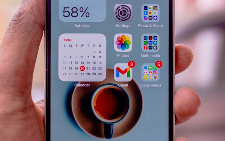 Hand holding a smartphone with app icons, battery percentage, and a calendar widget