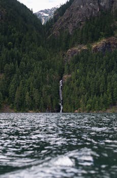 郁郁葱葱的绿色山地森林中，宁静的湖泊旁有瀑布