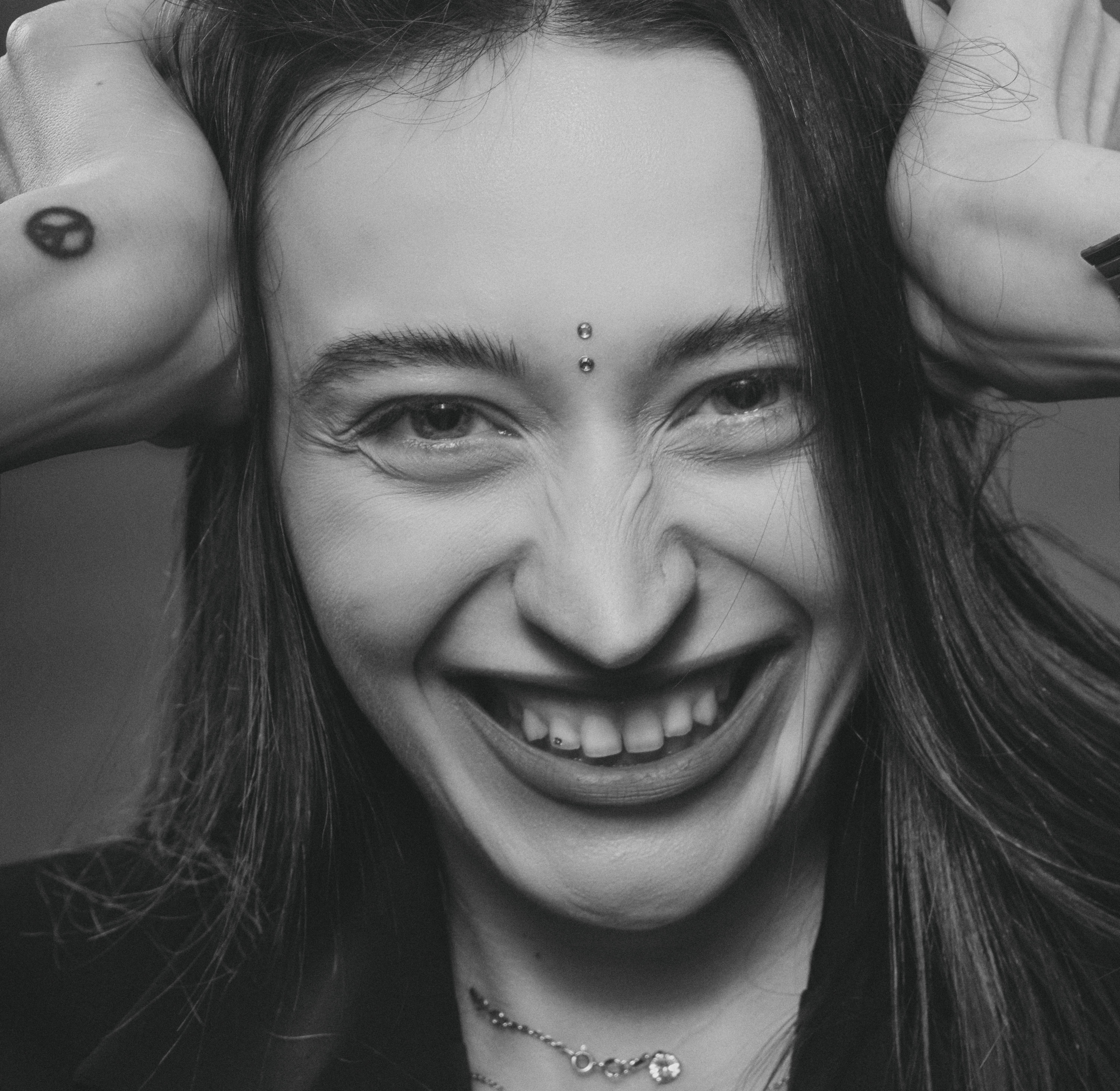 Candid close-up of a young woman with facial piercings smiling joyfully in black and white.