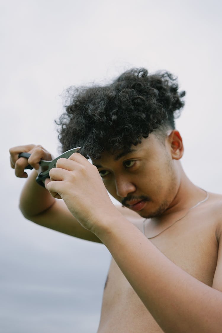 A Shirtless Man Cutting  His Hair 