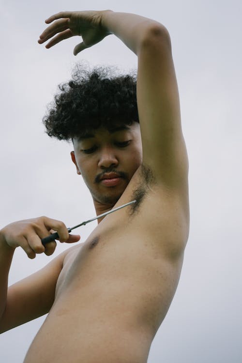 Photo of a Young Man Cutting His Armpit Hair with Scissors