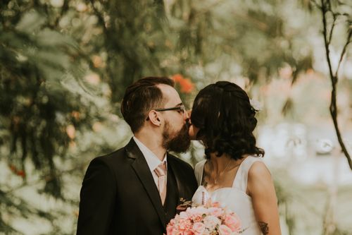 Free Bride and groom share a romantic kiss surrounded by lush greenery on their wedding day. Stock Photo