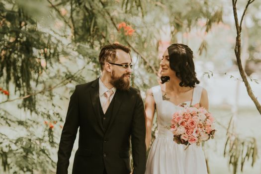 Bride and groom walking through a lush garden holding hands on their wedding day.