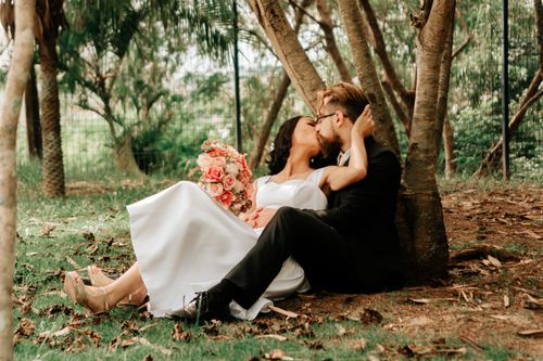 Free Charming couple in wedding attire shares a romantic kiss under trees in a park. Stock Photo