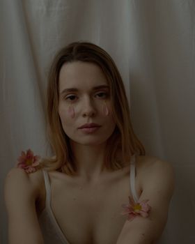 A young woman poses with floral accents against a white backdrop, creating a soft, dreamy aesthetic.