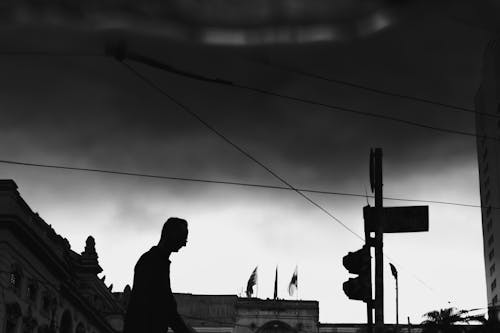 Silhouette of a Man Walking on a Street in City under a Cloudy Sky 