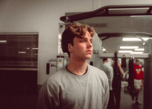 A young man in a gym setting, surrounded by fitness equipment, gazing thoughtfully.